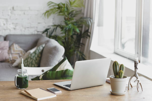 istock Workplace of modern freelancer leading healthy lifestyle: open generic laptop computer, cactus in pot, smart phone, copybook and glass of green smoothie on wooden desk in stylish home office interior 2198990538