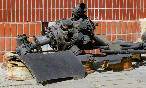 Old and weathered mechanical components lie on the ground beside a brick structure, showcasing their decayed state.