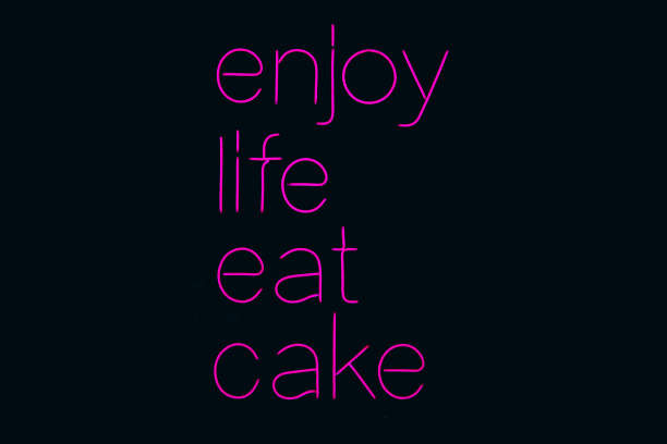 Neon sign phrase Enjoy life eat cake on black background isolated. A glowing neon sign that is often used in shop interior design.