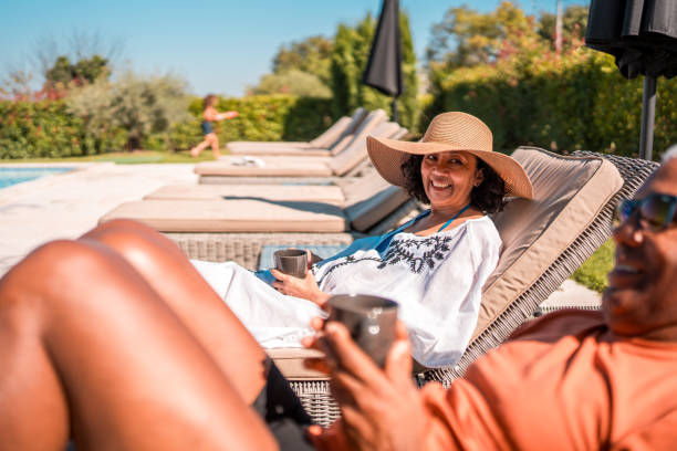 An elderly Hispanic man and woman enjoy a peaceful time by the pool while sitting on deckchairs.
