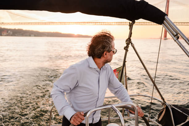 istock Man Steering Sailboat at Sunset with Lisbon Bridge in Background 2199014327