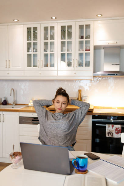 istock Female student stretches her arms, easing tension while studying online from home 2199016665