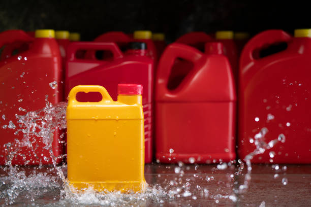 Front view of yellow plastic motor oil bottle splashed by stream of water, container with handle and red screw cap without label against background of red bottles