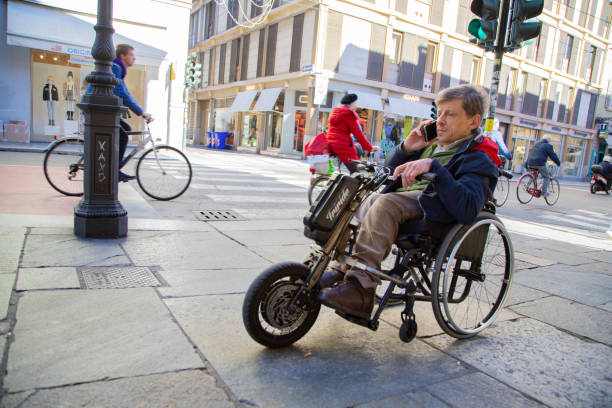 Parma, Italy, November 17, 2023: Disabled man in electric wheelchair struggles on busy city streets with traffic and pedestrians around him.