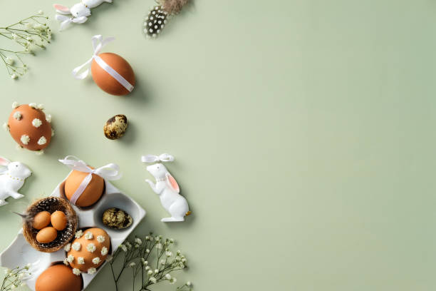 istock Easter flat lay composition with decorated eggs, ceramic bunnies, and flowers on a pastel green background 2199030497