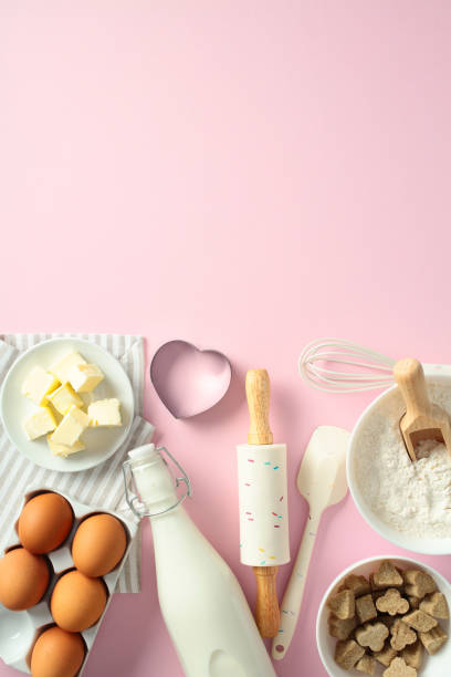 istock Baking ingredients and tools on a pink background: butter, eggs, milk, flour, brown sugar, rolling pin, whisk, spatula, and heart-shaped cookie cutter. Flat lay, top view. 2199030794