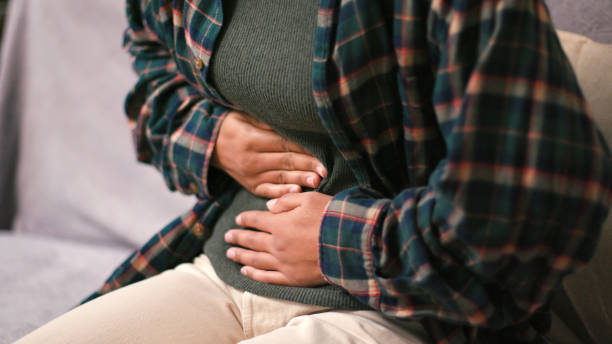 istock Upset Latin American woman bends massaging abdomen on sofa 2199030806