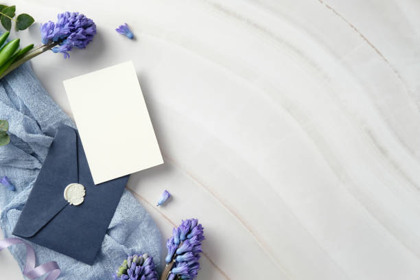 istock Elegant flat lay with blank white card on dark blue envelope, adorned with wax seal, surrounded by purple hyacinths and light blue fabric on marble background. 2199031064