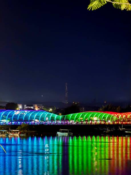 istock Illuminated Modern Pedestrian Bridge with Colorful LED Lights at Night, Reflected on Water – Urban Architecture, Landmark, Tourism, Travel, Cityscape, Nightscape, Reflection, Waterfront, and Neon Lights 2199032330