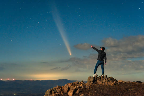 An Asian man stood on a mountaintop watching a comet embrace a comet called Tsuchinshan ATLAS (C/2023 A3) against the backdrop of stars.