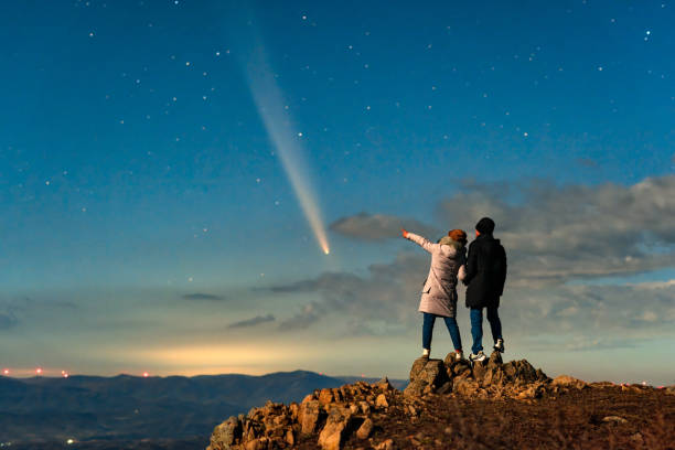 A couple stood on a mountaintop watching a comet embrace a comet called Tsuchinshan ATLAS (C/2023 A3) against the backdrop of stars.