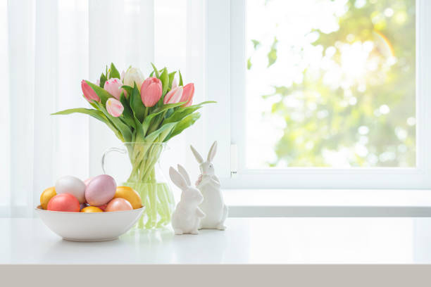 istock Easter eggs in bowl, fresh tulip flowers and ceramic bunny rabbits on blur spring window background 2199033424