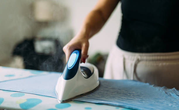istock Person Ironing Clothes with a Modern Steam Iron in a Bright Room 2199035264