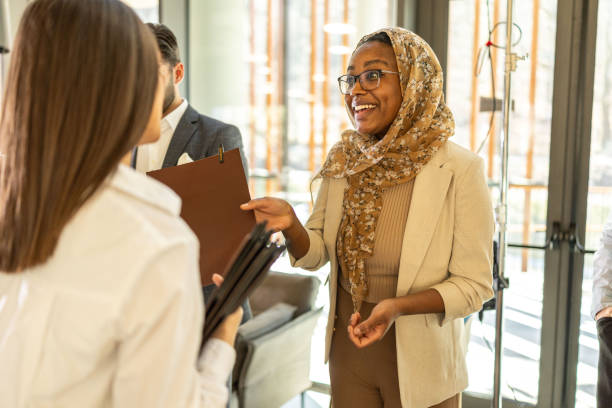 istock Smiling young female organizer sharing material to the members before the conference 2199035900