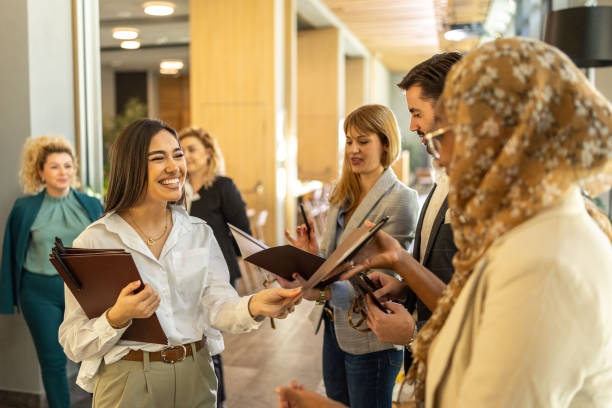 istock Smiling young female organizer sharing material to the members before the conference 2199035978