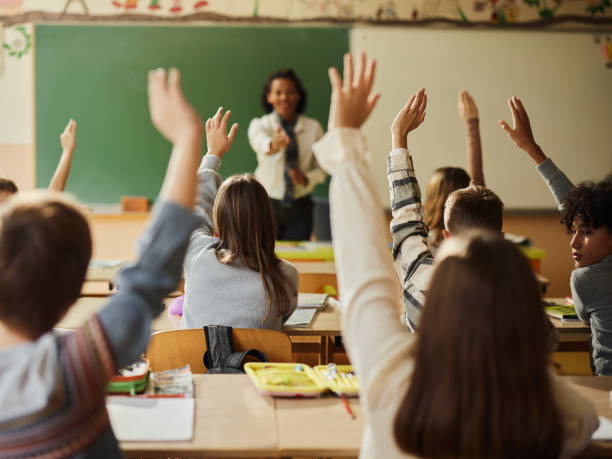 istock Back view of students raising their hands to answer the teacher's question on a class. 2199040028