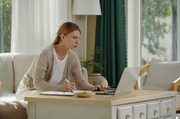 istock Woman Using Laptop and Taking Notes in Cozy Home Office 2199040809