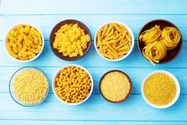 istock Assorted Uncooked Pasta in Bowls on Wooden Table 2199047070