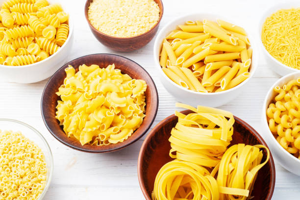 istock Assorted Uncooked Pasta in Bowls on Wooden Table 2199047074