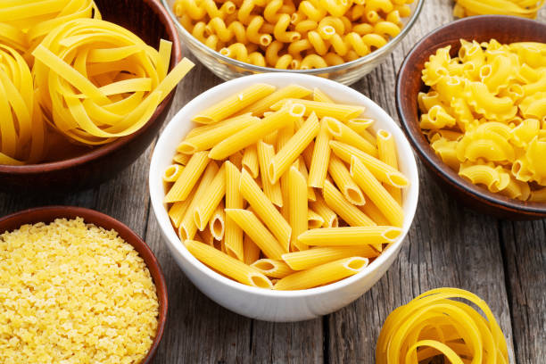 istock Assorted Uncooked Pasta in Bowls on Wooden Table 2199047081