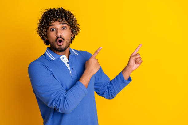 istock Young man with black curly hair gesturing on a yellow background, expressing surprise and enthusiasm, dressed in a blue shirt 2199048974