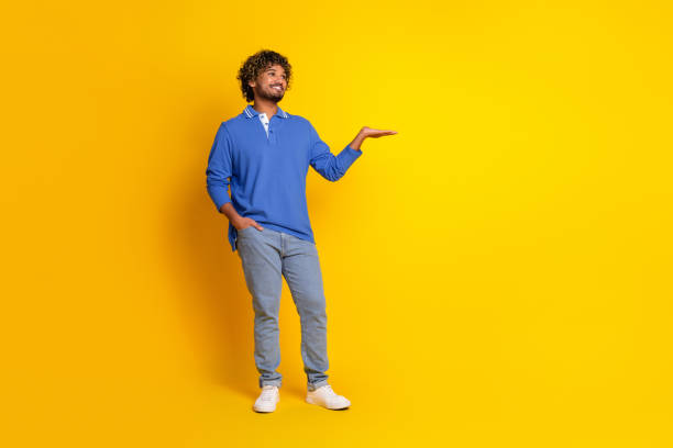 istock Stylish young man gesturing with his hand standing on a vibrant yellow background, wearing a casual blue polo shirt and jeans 2199049031