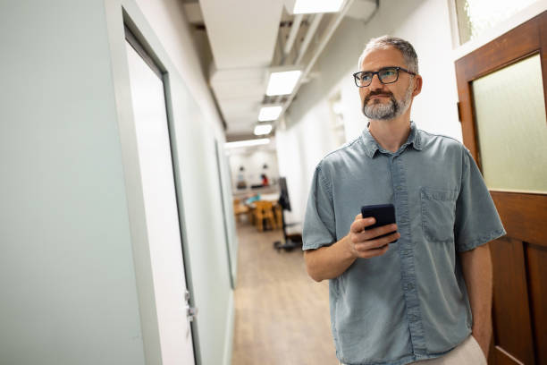 istock Man Holding Smartphone While Walking in a Modern Office Hallway 2199053609