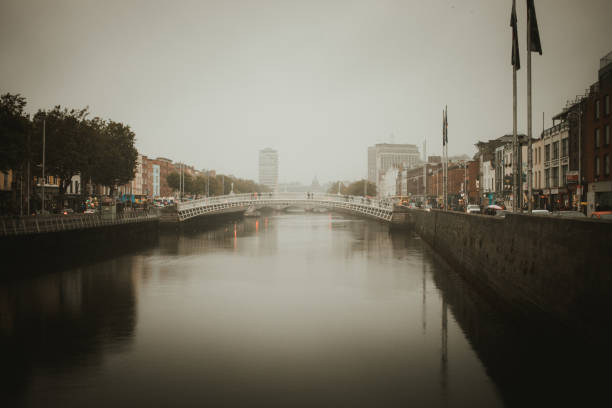 DUBLIN, IRELAND - SEPTEMBER 20, 2018: View of the Ha'penny Bridge spanning the River Liffey in Dublin on a misty day, with the cityscape and reflections on the water.