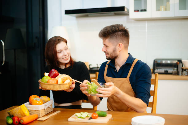 istock Young couple enjoys cooking together with fresh vegetables, fruit, and bread in a cozy kitchen. 2199056921