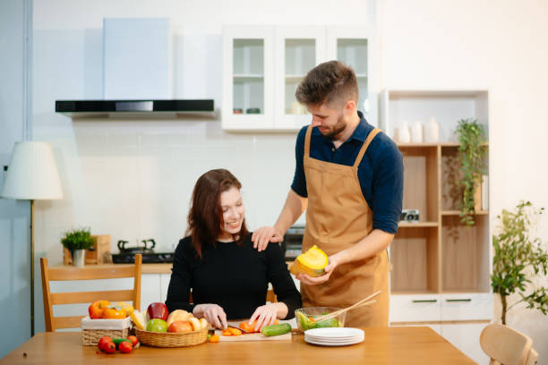 istock Young couple enjoys cooking together with fresh vegetables, fruit, and bread in a cozy kitchen. 2199056928