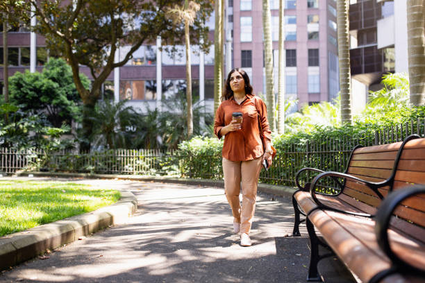 Person Walking Outdoors Holding a Coffee Cup in a Scenic Urban Park