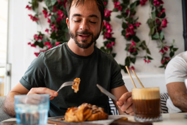 istock Man Enjoying a Pastry and Coffee at a Cafe With Floral Decor 2199059582