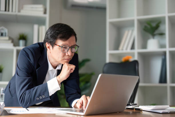 istock Elderly businessman deep in thought while working on a laptop in a modern office. 2199060789