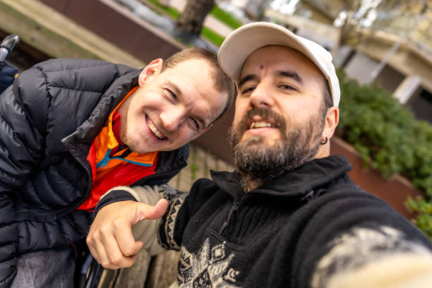 Young man having a happy video conversation on cellphone, sitting on a red park bench during a cold winter day