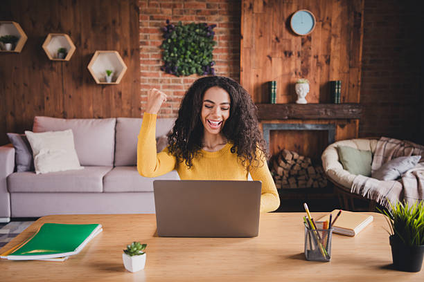 istock Excited young woman celebrating success while studying from home on a laptop, online learning in a cozy, natural light interior. 2199076234