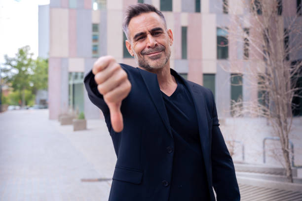 istock Business man pointing with thumbs down looking surprised at camera outdoors 2199079277