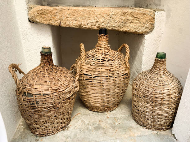 istock Three vintage wicker-covered glass demijohns placed against a rustic stone shelf and white plastered wall. 2199081061