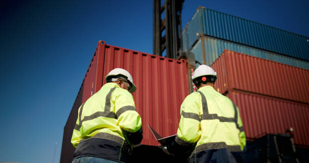 istock Two male dock managers standing and discussed over a laptop with engineer worker on the shipment in front of container box in the container warehouse area. Shipping Cargo Freights with Cargo Containers. Logistics import and export shipping yard. 2199085162