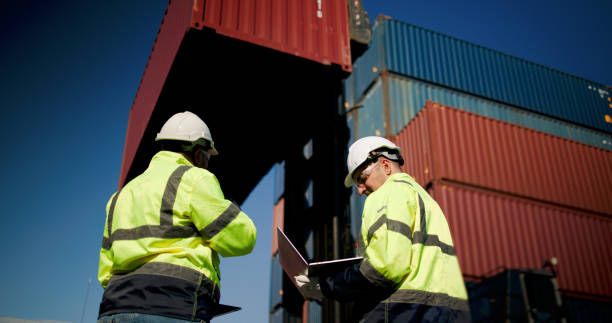 istock Two male dock managers standing and discussed over a laptop with engineer worker on the shipment in front of container box in the container warehouse area. Shipping Cargo Freights with Cargo Containers. Logistics import and export shipping yard. 2199085169