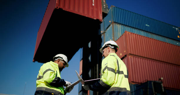 istock Two male dock managers standing and discussed over a laptop with engineer worker on the shipment in front of container box in the container warehouse area. Shipping Cargo Freights with Cargo Containers. Logistics import and export shipping yard. 2199085176