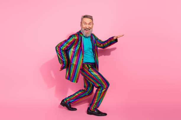 istock Charismatic elderly man posing playfully in a stylish rainbow-colored suit against a lively pink background 2199090374