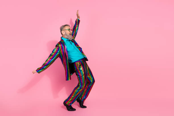istock Eccentric elderly man in colorful striped suit gleefully posing against a bright pink background 2199090380