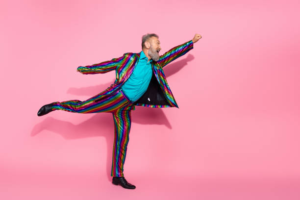 istock Charismatic senior man in vibrant rainbow suit posing playfully against pink backdrop conveying fun and eccentric style 2199090392