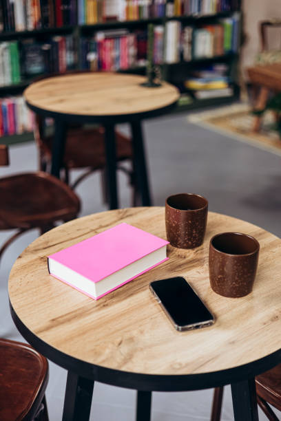 Pink book, smartphone and cups on table in bookstore cafe.