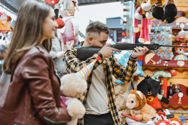 istock Boyfriend Holding Gun at Target Shooting Game Aiming With Focus Wanting to Impress Girlfriend 2199096104