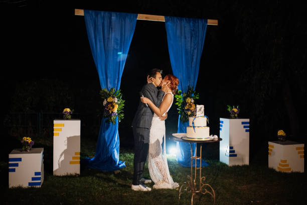istock young couple cutting cake against background of evening wedding arch 2199106953
