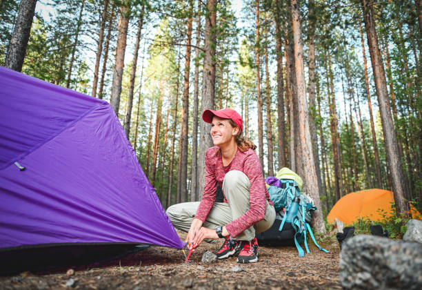 istock woman pitching a tent in a forest camp 2199109183