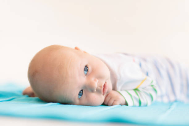 Adorable baby in white sunny bedroom. Newborn child relaxing in bed. Nursery for young children. Textile and bedding for kids. Family morning at home. New born kid during tummy time with toy bear.