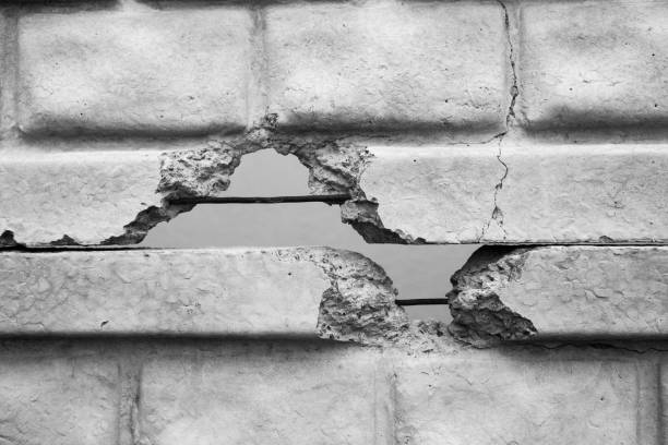 A concrete wall displays significant cracks, exposing underlying steel bars and textures.