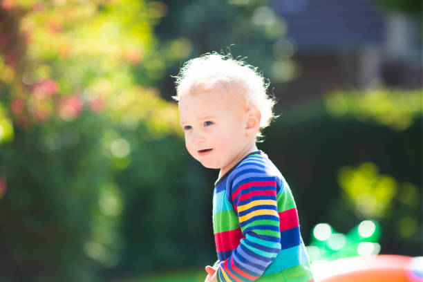 Child in summer park. Baby boy in spring garden. Kid playing outdoor. Curly blond toddler in rainbow shirt. Kids play in backyard.